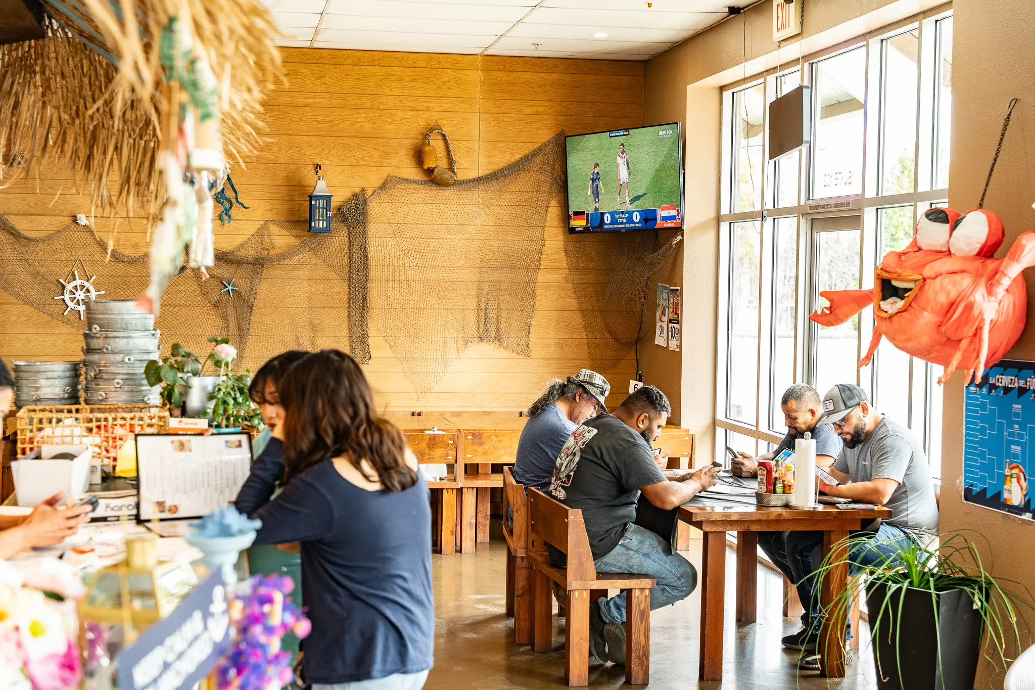 The Wacky Crab Shack dining room with families eating under a fishing-net-and-tiki ceiling, with soccer playing on the TV