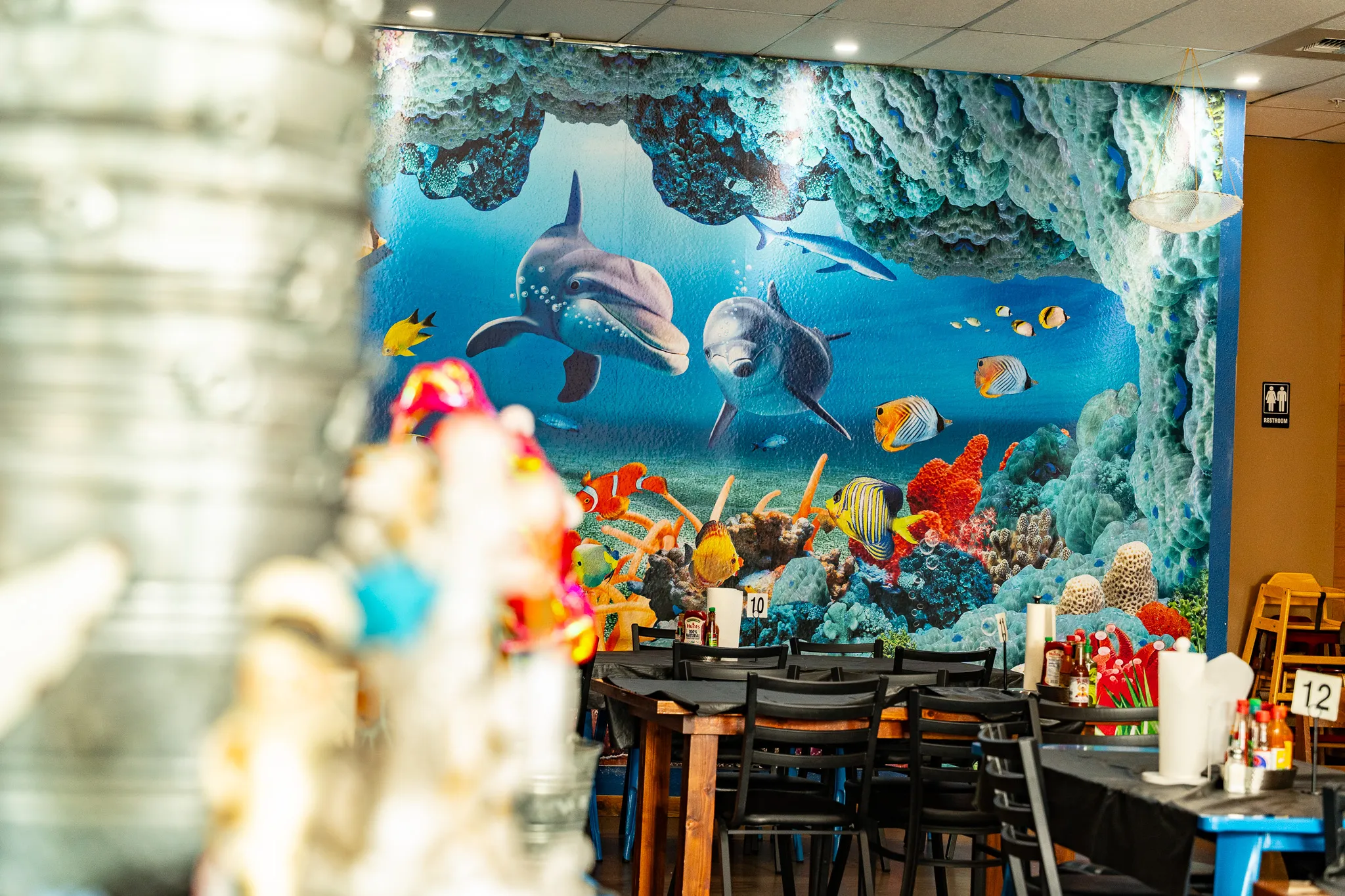 Wacky Crab Shack dining tables in front of the dolphin-and-coral reef mural, with colorful crab decor in the foreground