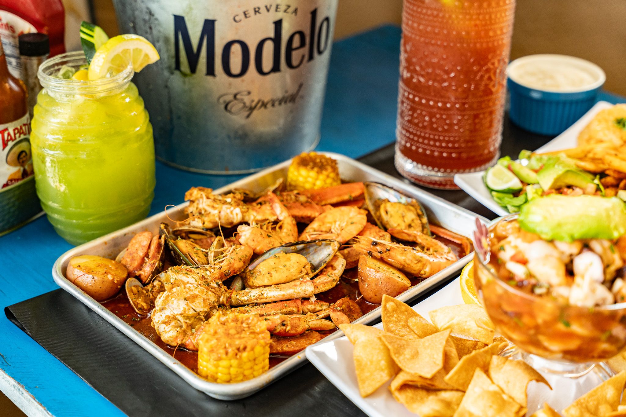 A Wacky Crab Shack seafood boil tray of shrimp, crab, clams, mussels, and corn, served with a Michelada and a green cocktail