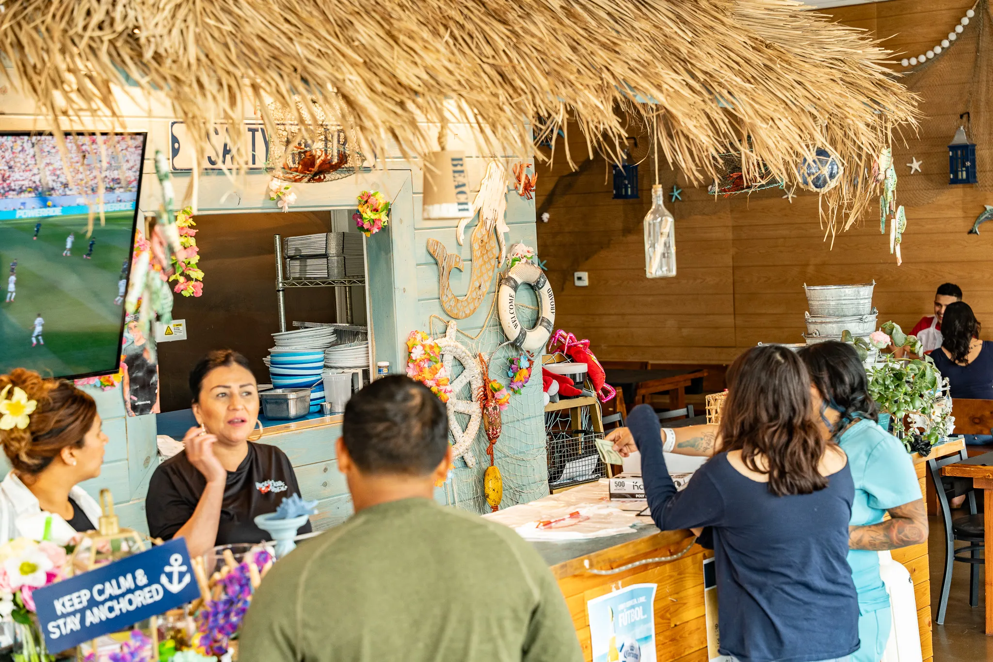The Wacky Crab Shack kitchen counter under a thatched tiki roof, where the team greets guests and takes orders