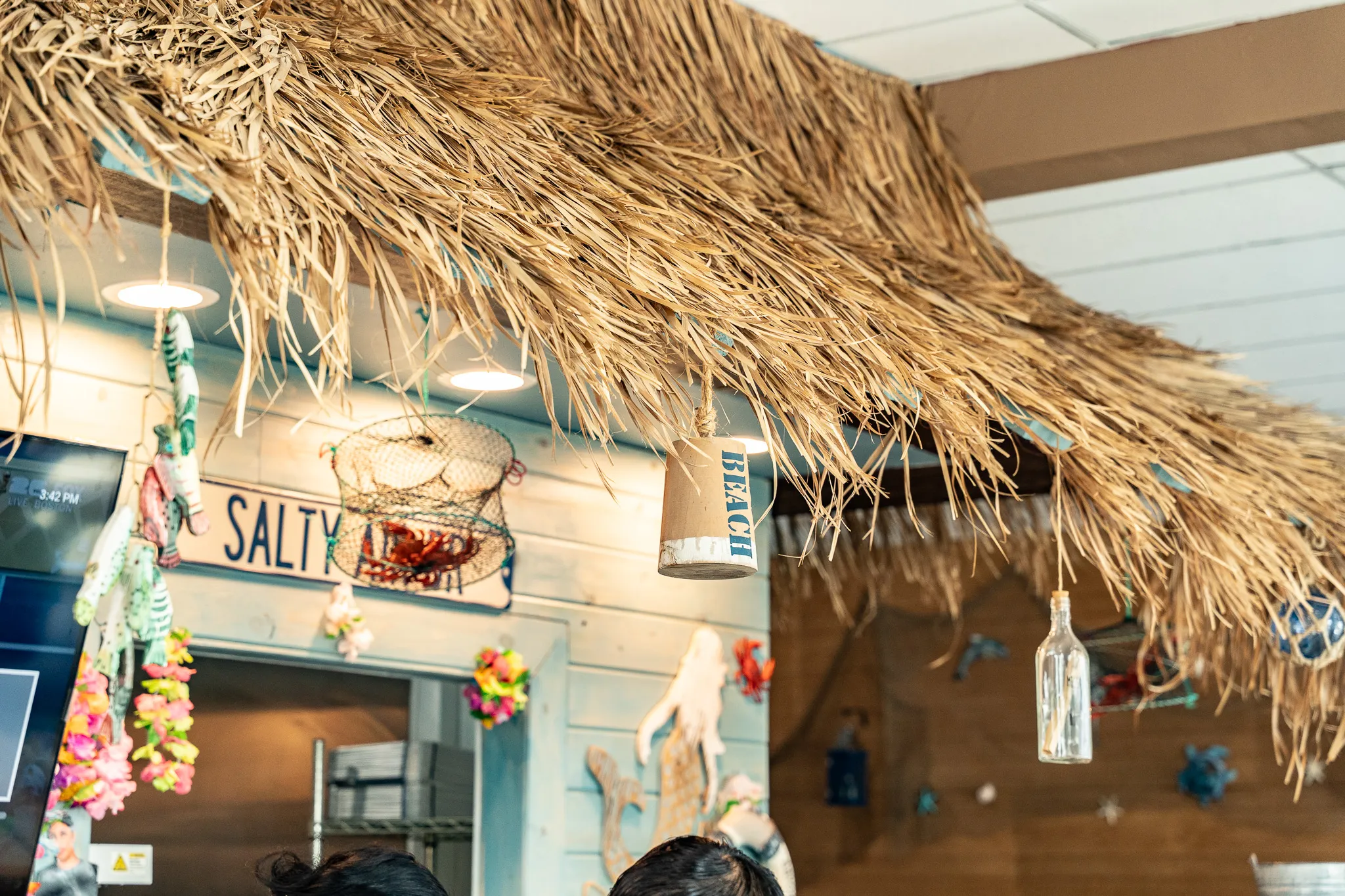 Detail of the thatched tiki roof and hand-painted "Salty Air" sign hanging over the Wacky Crab Shack counter